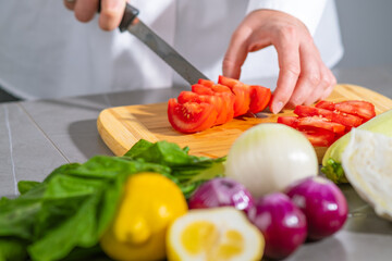 A person is preparing food by slicing tomatoes on a wooden cutting board