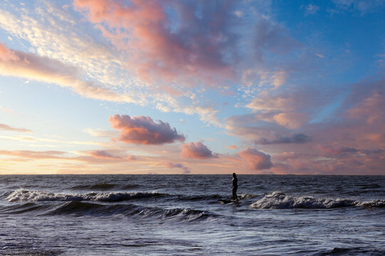 Beautiful and colorful silhouette of a surfer in the sun of dawn. Dramatic morning clouds over calm ocean waters with patient surfe