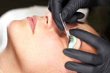  A beautician wearing black gloves meticulously applies eyelash extensions to a woman's lashes...