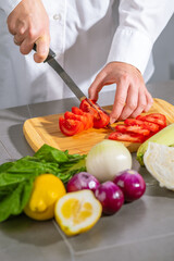 Woman in white shirt cutting vegetables on wooden cutting board, various vegetables laid out on table around