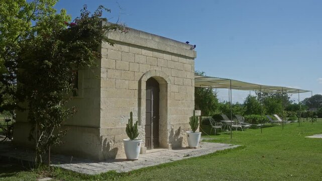 An outdoor stone building surrounded by greenery and chairs near a large pool under a clear blue sky in puglia, italy, europe.