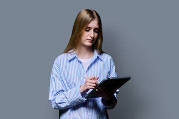 Teenage female student using digital tablet on gray studio background