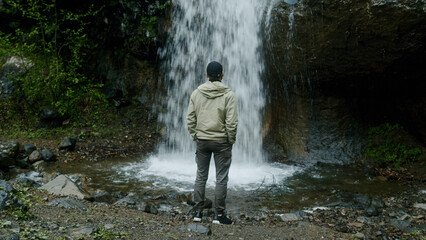 Young male traveler in enjoys a beautiful waterfall. Hiker man trekking, enjoying waterfall	
