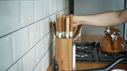 A person is selecting a knife from a wooden knife block in a modern kitchen, culinary preparation and home cooking. Kitchen tools, cooking routines, and domestic life.	

