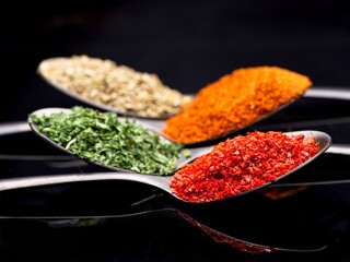 Various spices on black reflective surface.