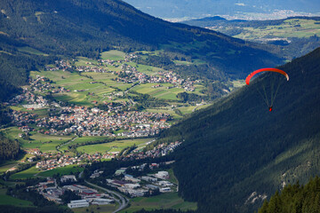 A paraglider descends towards an Austrian valley in the Stubai Alps, surrounded by majestic...