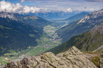 Scenic view of the Stubai Valley in the Austrian Alps on a sunny summer day with light clouds dotting the sky.