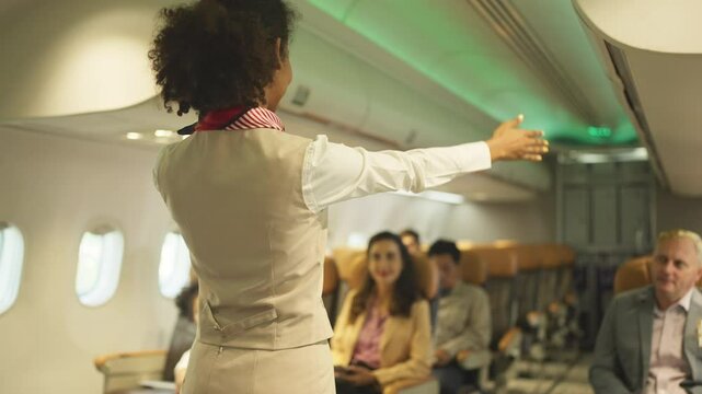 Back of Air hostess or airline staff woman demostrate and guide the emergency exit of airplane to the passenger before take of the flight to the other city.