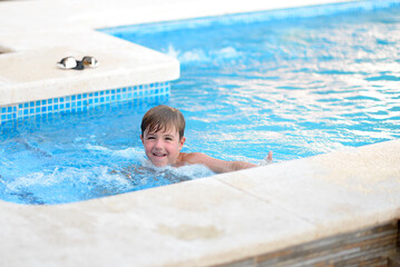 happy child swims into a pool with azure water, streams of jets of a filtration system on the...