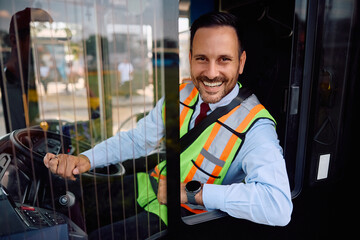 Happy public transport driver behind  wheel in bus cabin looking at camera.