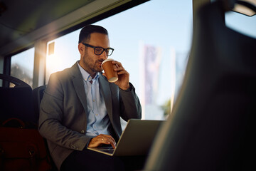 Male entrepreneur drinking coffee while using laptop in city bus