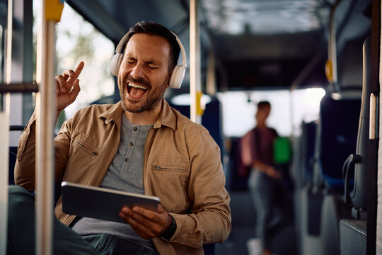 Cheerful commuter singing while using touchpad and listening music on headphones in a bus.