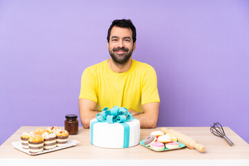 Man in a table with a big cake keeping the arms crossed in frontal position