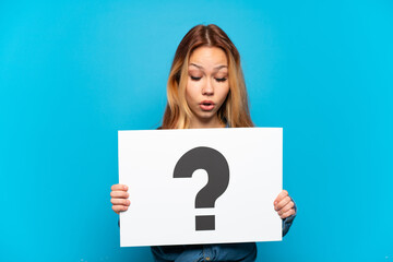 Teenager girl over isolated blue background holding a placard with question mark symbol