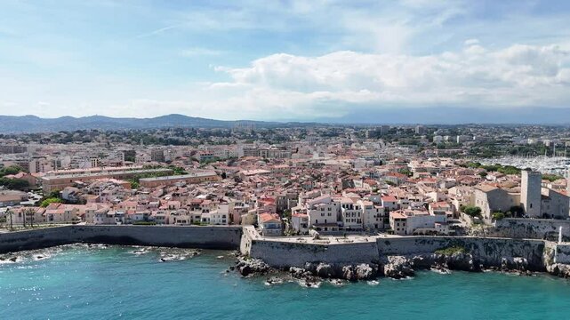 Drone shot of Antibes, France, featuring the beach, church, marina with boats, and the stunning C&ocirc;te d'Azur coastline along the Mediterranean Sea.