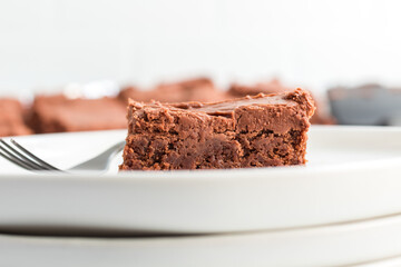 Single brownie with chocolate frosting on a white plate, close-up