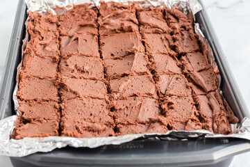 Brownies with chocolate frosting cut into squares in a baking pan