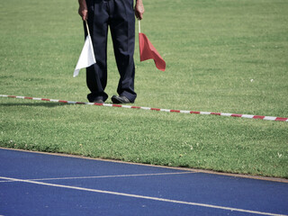 referee with two red and white flags standing in a track and field arena