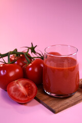 tomato juice with fresh tomatoes on a pink background. A fragrant drink.