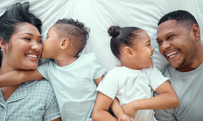 Fototapeta premium Above, happy and parents with children in bed for love bonding, care and kiss in family home. Smile, mother and father with kids on mattress for fun together, security and morning wake up in bedroom