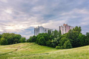 City park with rolling lawn, bushes and trees against the backdrop of multi-story buildings.