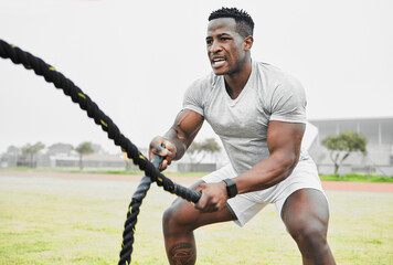 Battle rope, black man and fitness with workout for strong arm muscle development, endurance and intensity on field. Male athlete, exercise and heavy cord in sports ground for conditioning and power