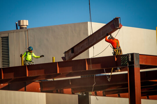 A consruction worker directing placement of a large steel beam that is atttached to a crane