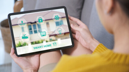 Hand using digital tablet with smart home control icon on screen while sitting on sofa at home, smart home control concept

