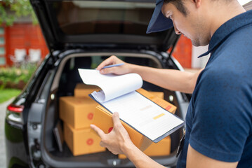 A delivery man wearing a hat and uniform checks the customer's address. Cardboard boxes near delivery truck to customer's home The postman is delivering a parcel.