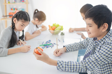 Asian boy use hand holding tomato, asian children group training to drawing and paint image, they feeling happy and smile, they use pencil and crayon color in art training time