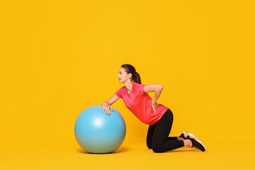 Beautiful pregnant woman doing exercises with fitball on yellow background