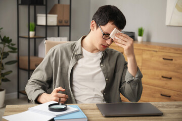 Embarrassed man with tissue at wooden table in office