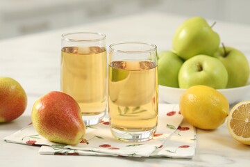 Glasses of fresh juice and fruits on white marble table in kitchen