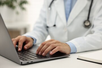 Fototapeta premium Doctor using laptop at white table in hospital, closeup