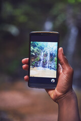 Hands, phone screen and waterfall in nature for photography, social media and adventure. Mountain, person and hiking for travel or vacation in mountains with journey, memory and online for post