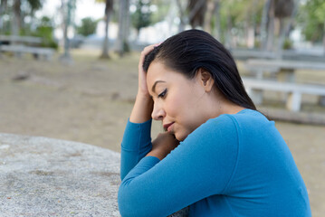 Woman seated in a public park with an attitude of preoccupation, pensive.