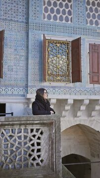 A young woman wearing glasses explores historical turkish architecture with intricate tilework and carvings at the topkapi palace in istanbul.
