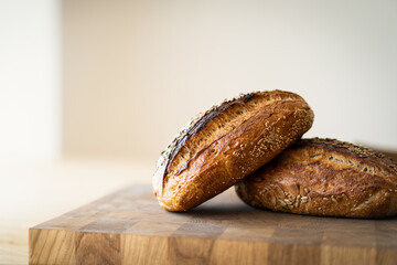 Two loaves of sourdough bread, freshly baked and still warm, are stacked on a wooden surface. The...