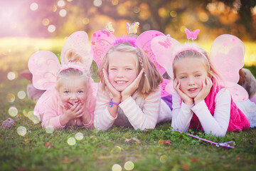 Outdoor, fairy and portrait of sisters lying in field with wings for dress up, princess outfit or cosplay. Bokeh, nature and young children with smile for fantasy play, childhood or halloween costume © AK Coop/peopleimages.com