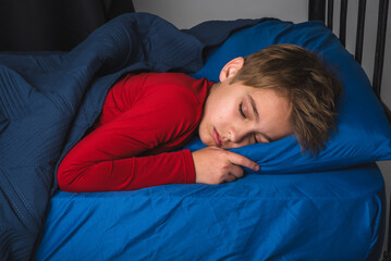 Young preteen boy sleeping in bed wearing red pajamas