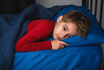Young preteen boy laying awake in bed wearing red pajamas © 303Photos.com