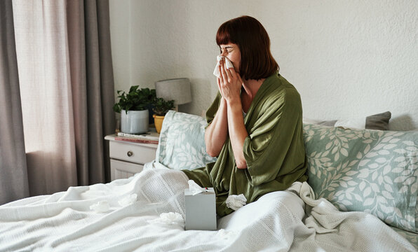 Woman, blowing nose and sick in home, allergies and tissue for illness or cold influenza in bedroom. Female person, sinusitis and recovery from virus or hayfever, bed and infection of flu or covid