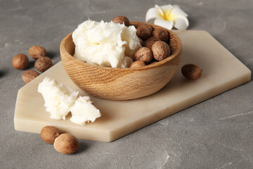 Bowl of shea butter with nuts and plumeria flower on grey background