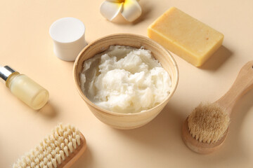 Bowl of shea butter with bottle of cosmetic oil, soap bar and massage brushes on beige background