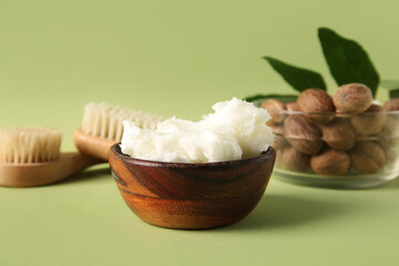 Bowls of shea butter and nuts on green background