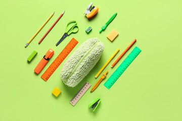 Naklejka premium Pencil case with different stationery on green background. Top view