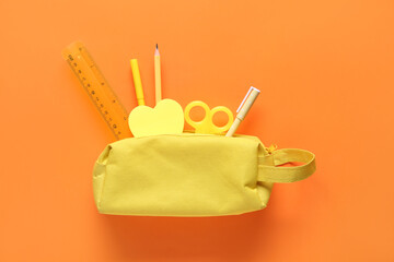 Yellow pencil case with different stationery on orange background. Top view