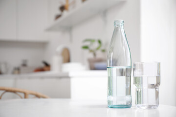 Bottle of water with glass on table in kitchen, closeup
