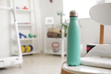 Bottle of water with towel on chair in gym, closeup