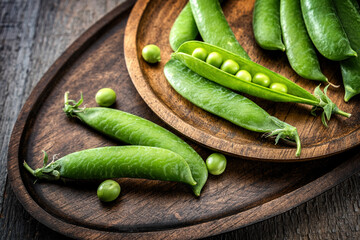 Bright, fresh green peas in pods on wooden plates, trays, close-up, rustic.